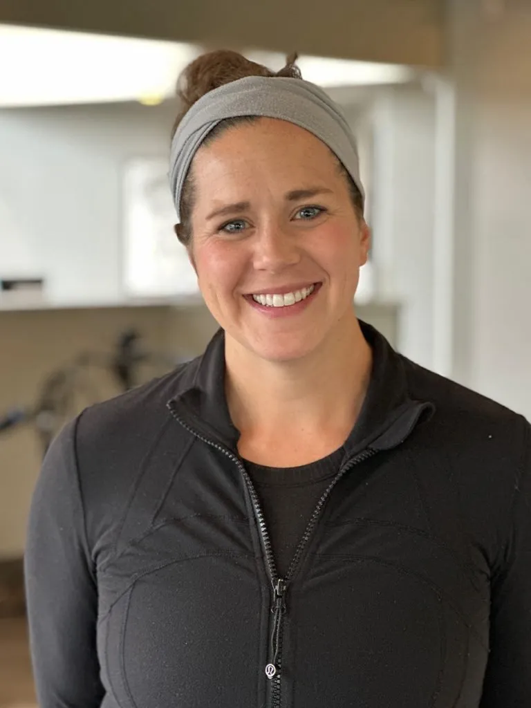 Smiling woman wearing a gray headband and black zip-up jacket indoors.